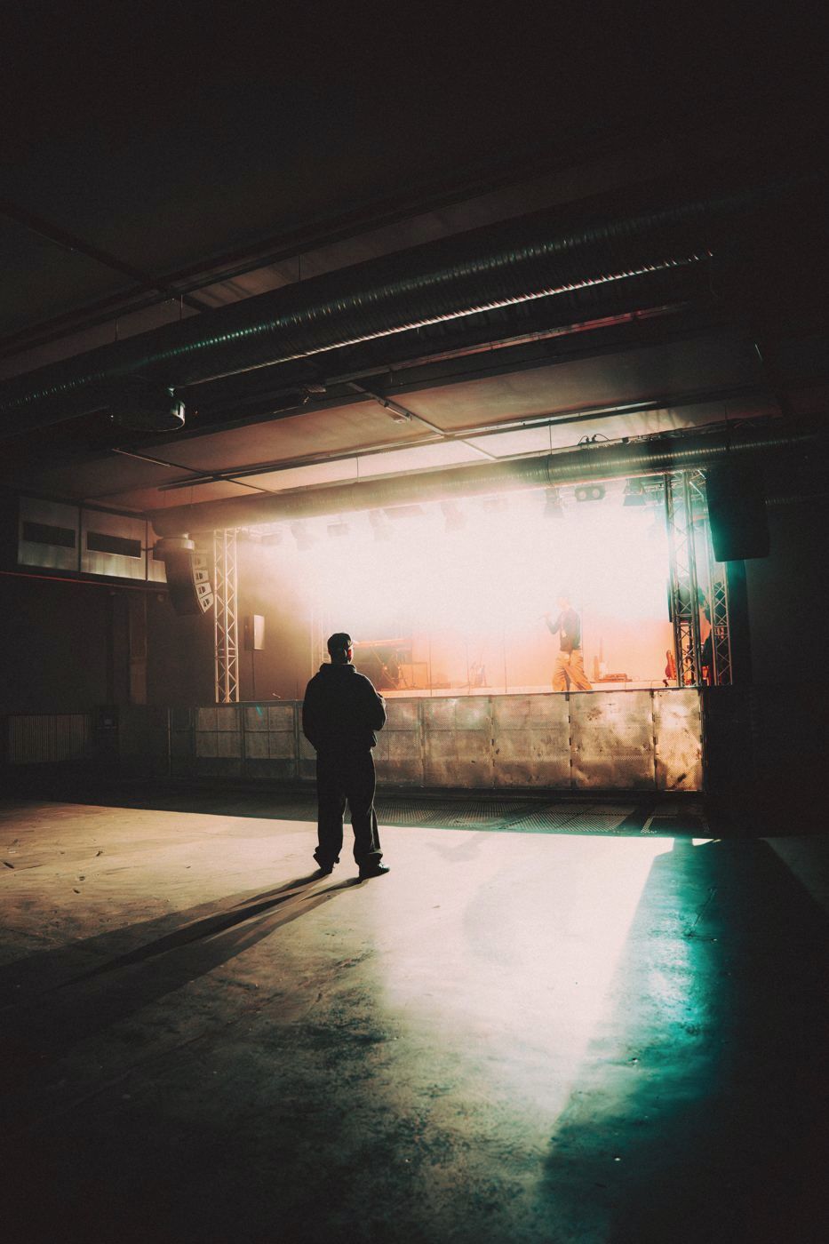 Silhouette einer Person vor einer hell erleuchteten Bühne in einer leeren Halle