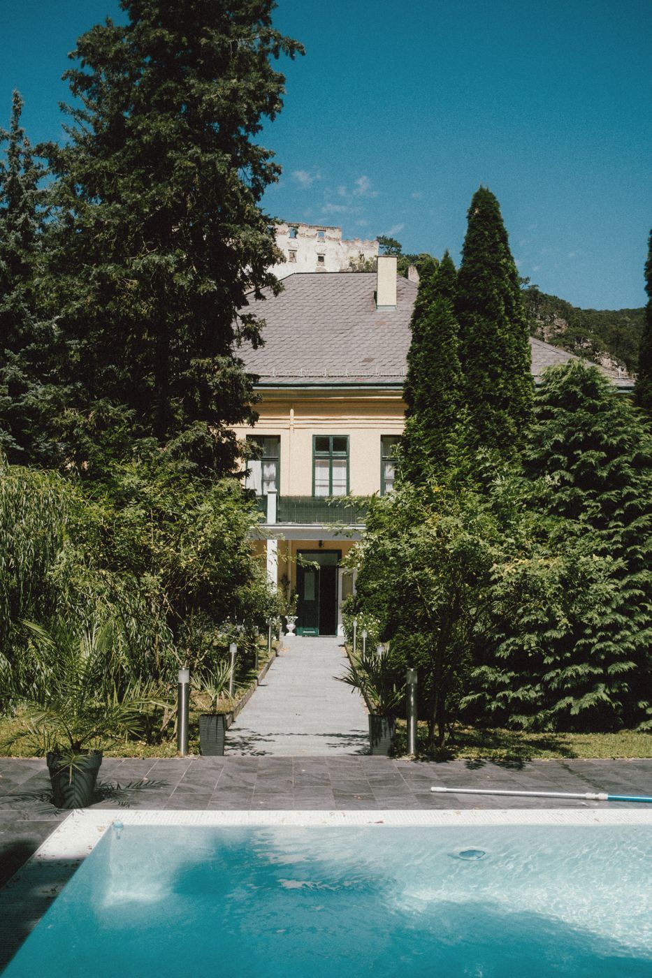 Villa im Grünen mit Pool im Vordergrund an einem Sommertag